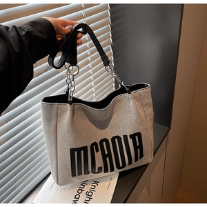 Detail of woven canvas tote with MCAOIA lettering, leather straps and metal chains