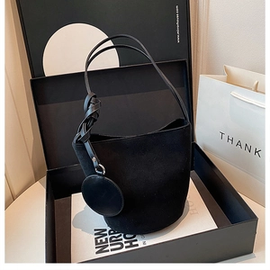 Détail d'un sac seau en daim noir avec poignée nouée présenté dans une boîte cadeau chic