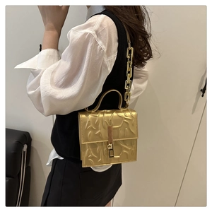 Detail of golden handbag with embossed texture, metal chain strap and rotating lock