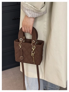 Close-up of brown quilted handbag featuring gold circular handles and a key charm pendant