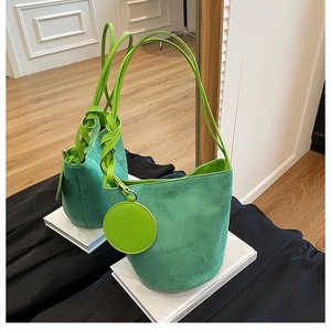 Gros plan d'un sac seau en daim vert avec un charme rond assorti et une poignée en cuir