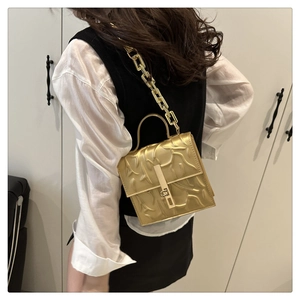 Detail of gold embossed handbag showing chain strap and metallic textured surface