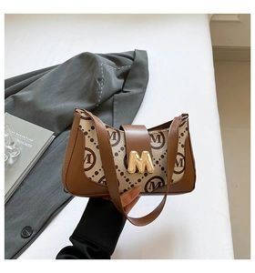 Close-up of vintage printed underarm bag with golden M buckle on white fabric