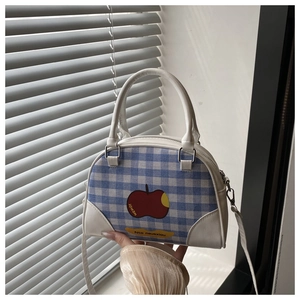 Close-up of blue plaid crossbody bag with red apple print and white handles