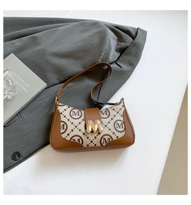 Detailed close-up of retro monogram canvas shoulder bag with gold M-shaped metal buckle