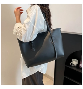 Close-up of minimalist black leather tote bag with vertical strap and long shoulder handles