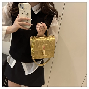 Detail of gold textured square handbag with metallic handle and thick chain strap