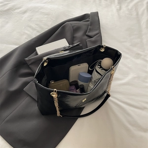 Large black patent leather tote bag with gold chain strap and spacious interior capacity