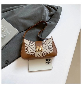 Close-up of vintage printed baguette bag with gold M-buckle next to a smartphone