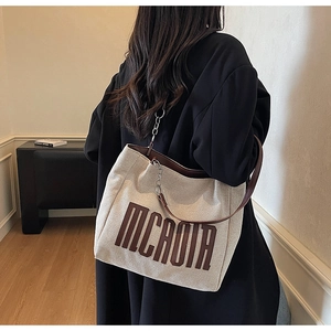 Macro shot of minimalist canvas tote with MCAOIA lettering and leather chain strap