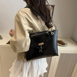 Chic black glossy shoulder bag with gold chain and deer pendant shown on a model