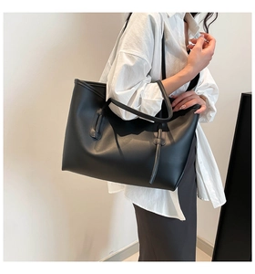 Side view of a large black leather tote bag with long straps worn by a model