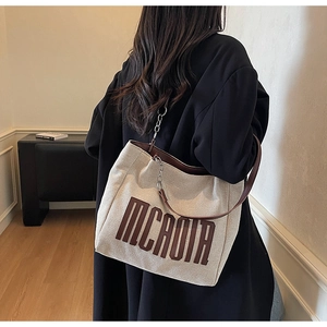 Detail of canvas tote bag with leather straps, chain decor and MCAOIR lettering print