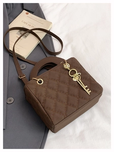 Detail of dark brown quilted crossbody bag with a golden key charm on a suit background
