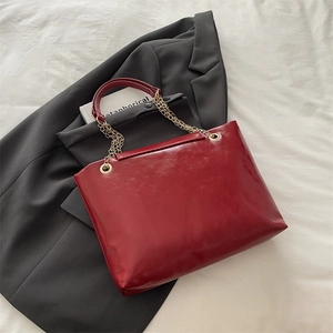 Red oil wax leather tote bag with gold chain strap on a blazer backdrop