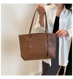 Detail of dark brown tote bag with slim handles and vertical stitching on model
