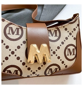 Detail of vintage canvas baguette bag with golden M metal clasp and brown leather texture