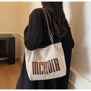 Detail of off-white canvas tote bag featuring brown 3D letters and leather strap