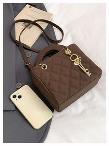 Detail of dark brown quilted rhombic stitching bag with gold key pendant and handle