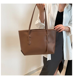 Detail of a large dark brown tote bag being held by a model for a daily commute look