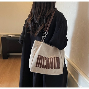 Detail of beige canvas tote bag with MCADIA logo and leather chain strap on a model