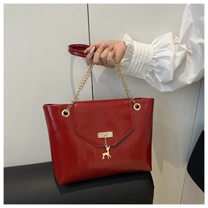 Close-up of shiny red leather handbag with golden elk charm and chain handle detail