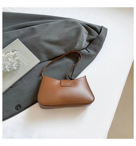 Detailed side view of a brown vintage baguette shoulder bag on white surface