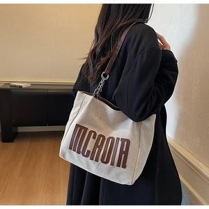 Detail of canvas tote bag with MCAOIA lettering, leather strap and metal ring connection