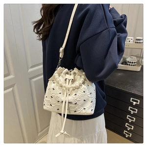 Détail du sac seau blanc avec anse en perles, nœud noir et texture plissée sur modèle
