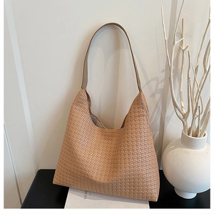 Detail of light brown woven leather tote bag with thick strap in a minimalist setting