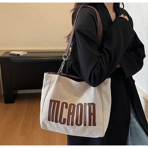 Detail of canvas tote bag with brown leather MCAOIR letter patches and metal chain strap