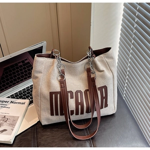 Canvas tote bag detail with MICADA lettering, leather handles, and metal chain accent
