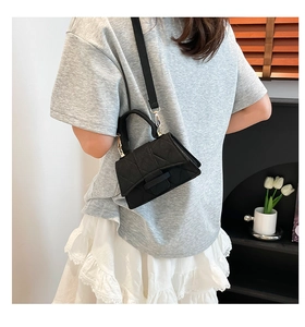Detailed view of a black quilted felt crossbody bag worn by a model in a minimal room