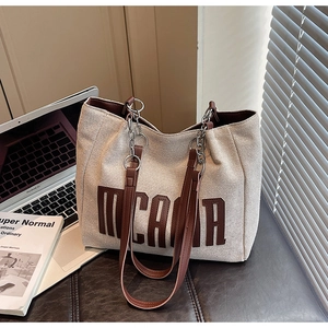 Detail of canvas tote bag showing brown leather straps and metallic chain connections