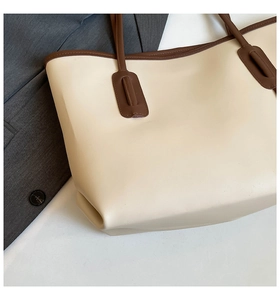 Close-up of beige tote bag with brown contrast trim on professional blazer background