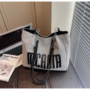 Close-up of grey canvas tote bag with black leather straps and metal chain link detail
