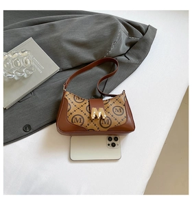 Detail of vintage baguette bag with M monogram pattern and gold metal clasp on a jacket