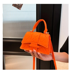 Detailed view of bright orange quilted handbag with velvet texture and golden hardware