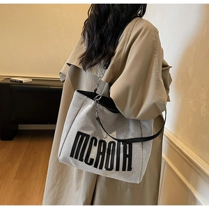 Detail view of large canvas tote bag featuring black letter print and sleek leather straps