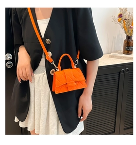 Detail of bright orange quilted crossbody bag with top handle and secure metal clasp