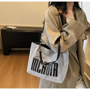 Detailed view of grey canvas tote bag with black letter embroidery and chain strap