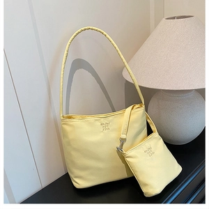 Detail of pale yellow nylon bucket bag set featuring minimalist embroidery and mini pouch