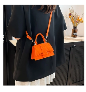 Detail of a vibrant orange quilted handbag with a matching handle and adjustable strap