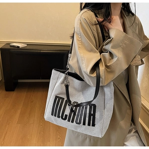 Detail of grey canvas tote with black MCKAUIR embroidery and metal chain strap