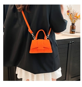 Detail of bright orange quilted crossbody bag styled on a black blazer with gold hardware