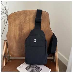 Close-up of durable black nylon crossbody bag with silver M logo on a wooden chair