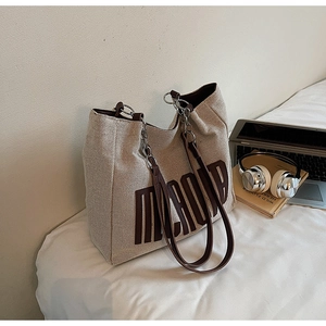 Detail of canvas tote bag with brown leather handles and silver chain on a white bed