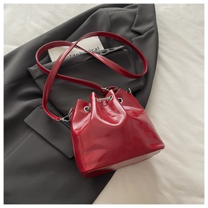 Detail of red glossy bucket bag with drawstring closure on a dark grey blazer