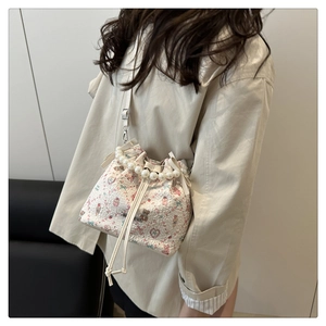 Détail d'un sac seau blanc à fleurs avec poignée en perles et nœud porté par un mannequin