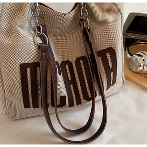 Detail of cream woven tote bag with brown leather letter patch and metal chain strap